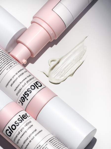 A closeup shot of three bottles of Glossier Universal ProRetinol and a product swatch on an offwhite background